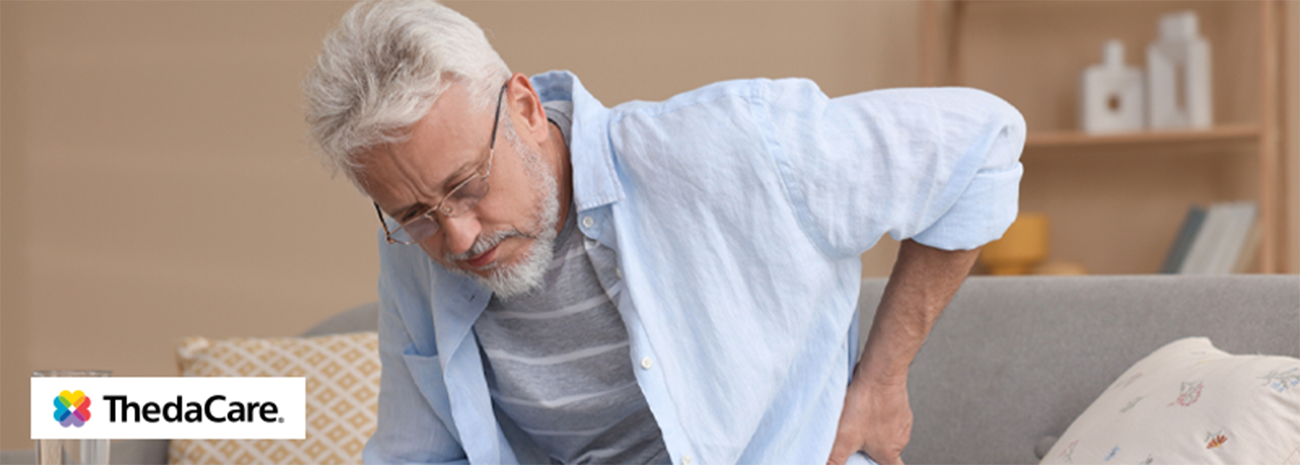 Senior man sitting on couch with his hand on his lower back in discomfort