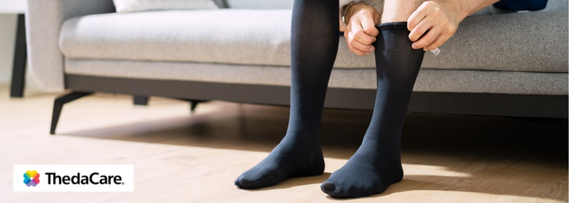 Man sitting on couch and pulling on black compression stockings