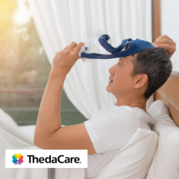 Man sitting up in bed in the morning removing his CPAP mask looking refreshed