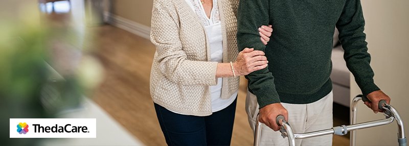 Senior woman walking with senior man that is using a walker