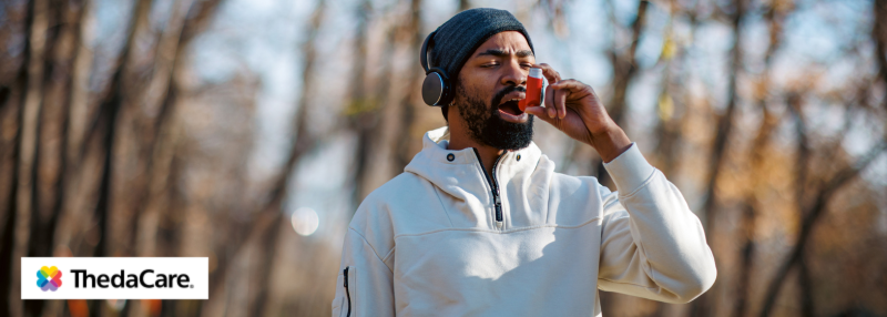 Man walking outside in the cold with headphones on while using an inhaler