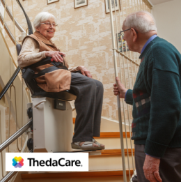 Elderly woman using stair lift to come down the stairs and elderly man watching contently 