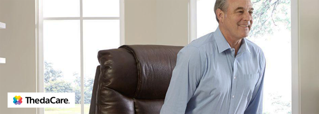 Image shows smiling older man standing up from lift chair in indoor setting