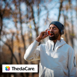 Man walking outside in the cold with headphones on while using an inhaler