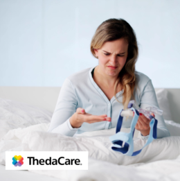 Woman sitting in bed looking frustrated at the CPAP mask in her hand