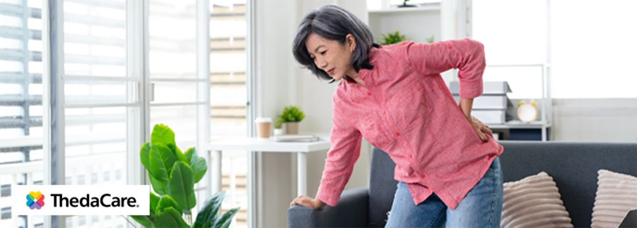 Older woman leaning forward and bracing on the couch with a hand on her back