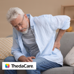 Senior man sitting on couch with his hand on his lower back in discomfort