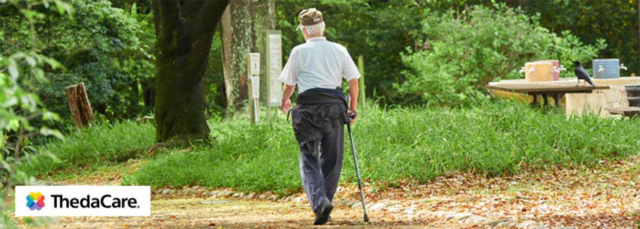 Elderly man walking outdoors on a trail with a cane in his hand