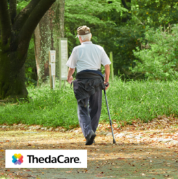 Elderly man walking outdoors on a trail with a cane in his hand