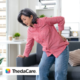 Older woman leaning forward and bracing on the couch with a hand on her back