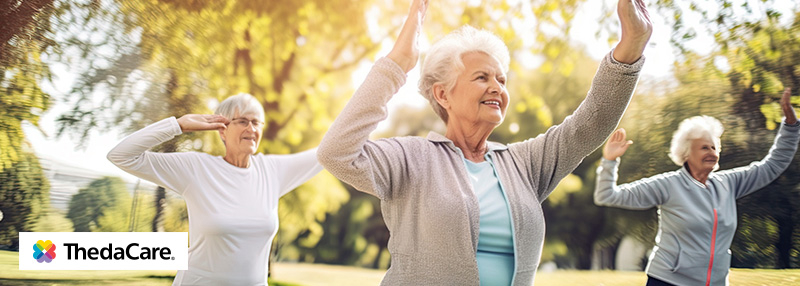 Elderly women outside exercising with their hands up in the air