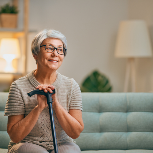 Senior woman smiling while sitting on couch with hands on a cane